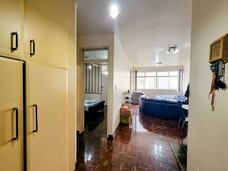 Open plan living area featuring traditional parquet flooring, built-in storage cabinetry, and natural light through large windows, connecting to adjacent bedroom space.