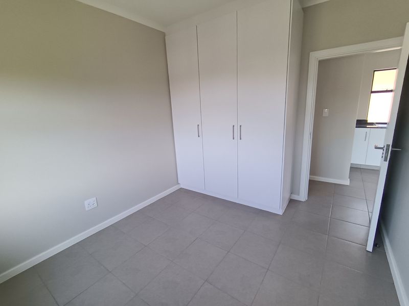 A clean, empty bedroom featuring neutral wall tones, tiled flooring, and a modern built-in wardrobe, offering a versatile space ready for personalization.