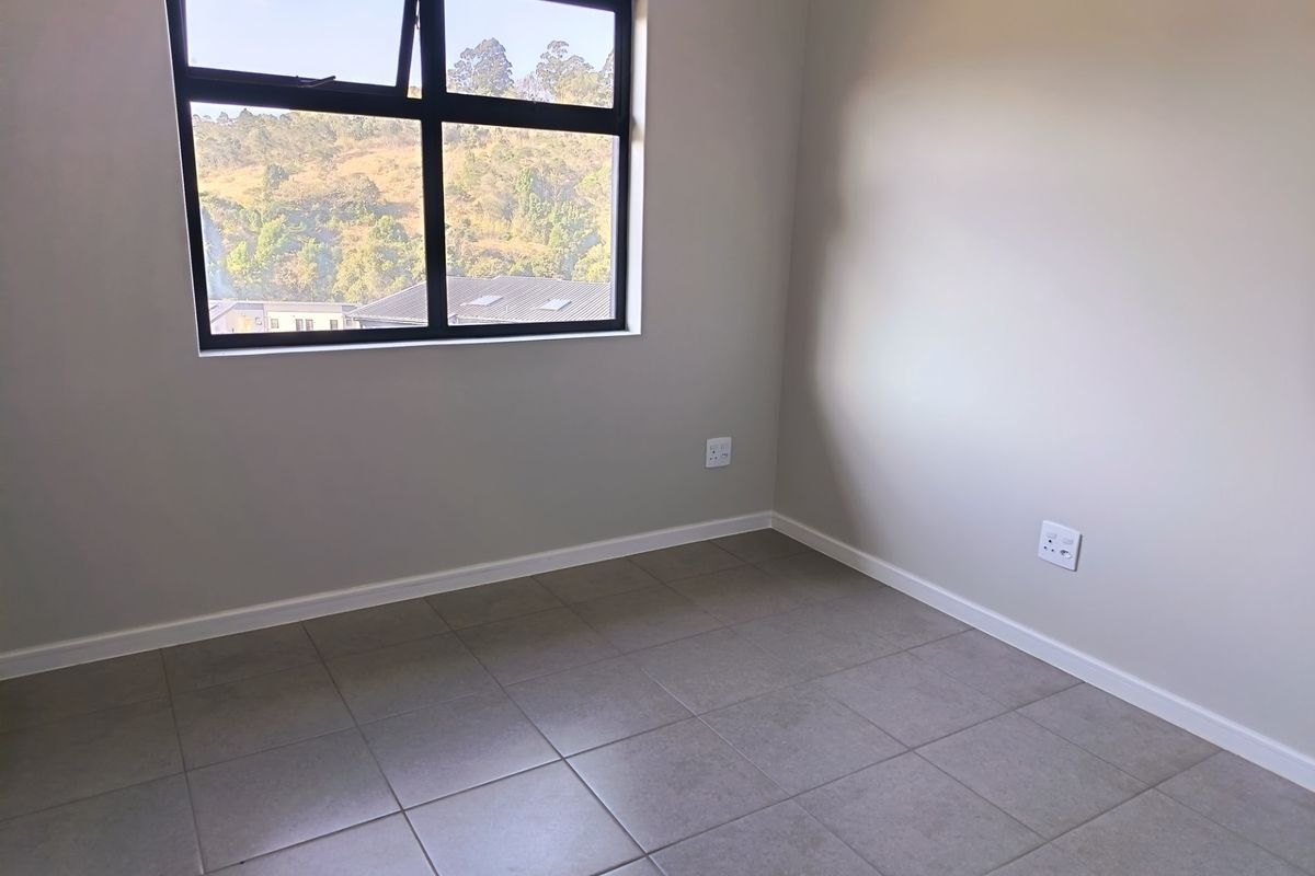 A clean, empty bedroom featuring neutral tiled flooring, modern aluminium window frames, and a bright, minimalist aesthetic ready for furnishing.