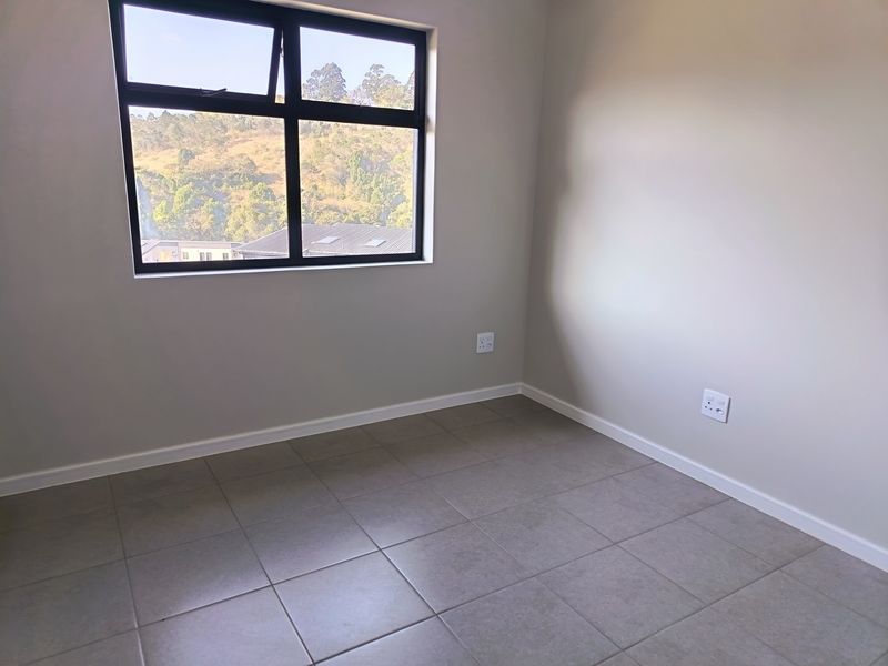 A clean, empty bedroom featuring neutral tiled flooring, modern aluminium window frames, and a bright, minimalist aesthetic ready for furnishing.