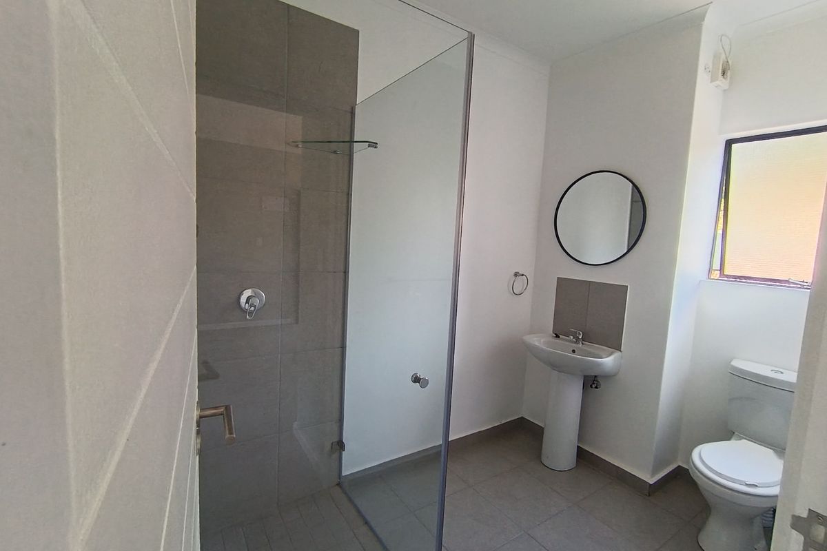 A clean, modern bathroom featuring a walk-in shower with glass screen, pedestal basin, and toilet, finished with neutral floor and wall tiling.