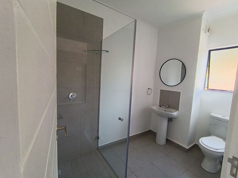 A clean, modern bathroom featuring a walk-in shower with glass screen, pedestal basin, and toilet, finished with neutral floor and wall tiling.
