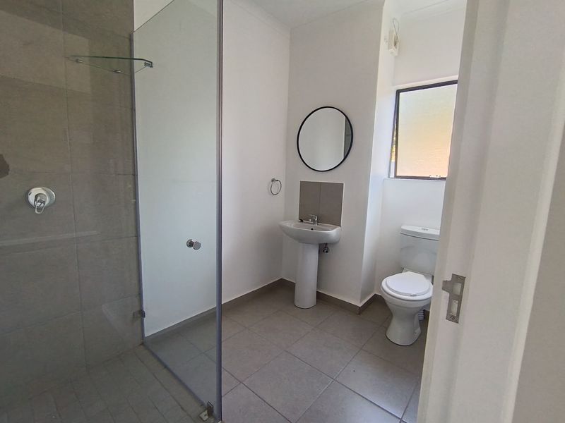A clean, modern bathroom featuring a tiled shower enclosure with a glass screen, a pedestal basin, and a standard toilet.