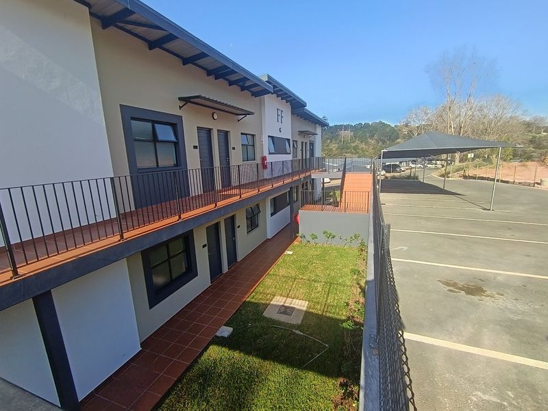 Exterior view of an apartment complex featuring a tiled walkway, metal balustrades, and adjacent covered parking bays.