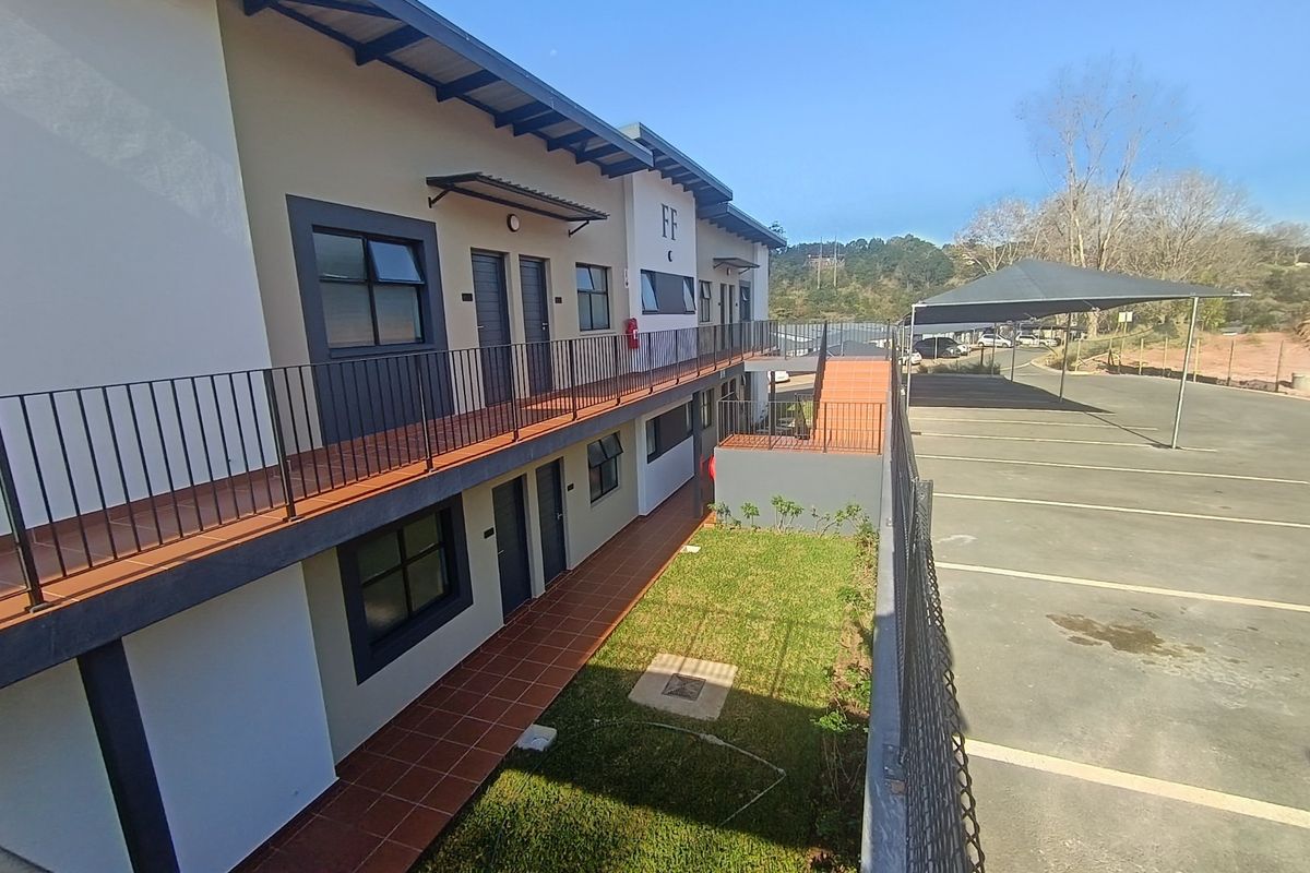 Exterior view of an apartment complex featuring a tiled walkway, metal balustrades, and adjacent covered parking bays.