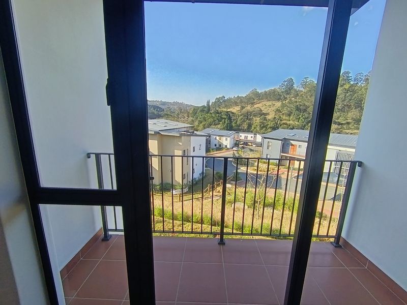 A clean, tiled balcony featuring a metal balustrade and offering an elevated view of the surrounding residential complex and hillside.