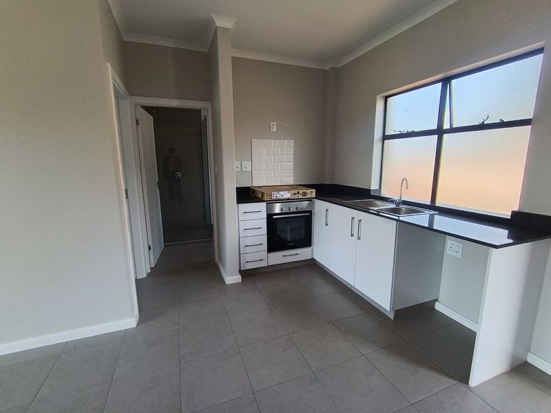 A clean, modern kitchen featuring white cabinetry, granite countertops, a built-in oven, and tiled flooring, offering a functional and neutral space.