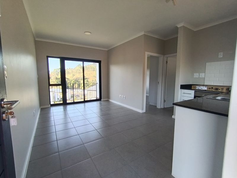 An open-plan living area featuring tiled flooring, a modern kitchen with granite countertops, and a sliding door leading to a balcony.