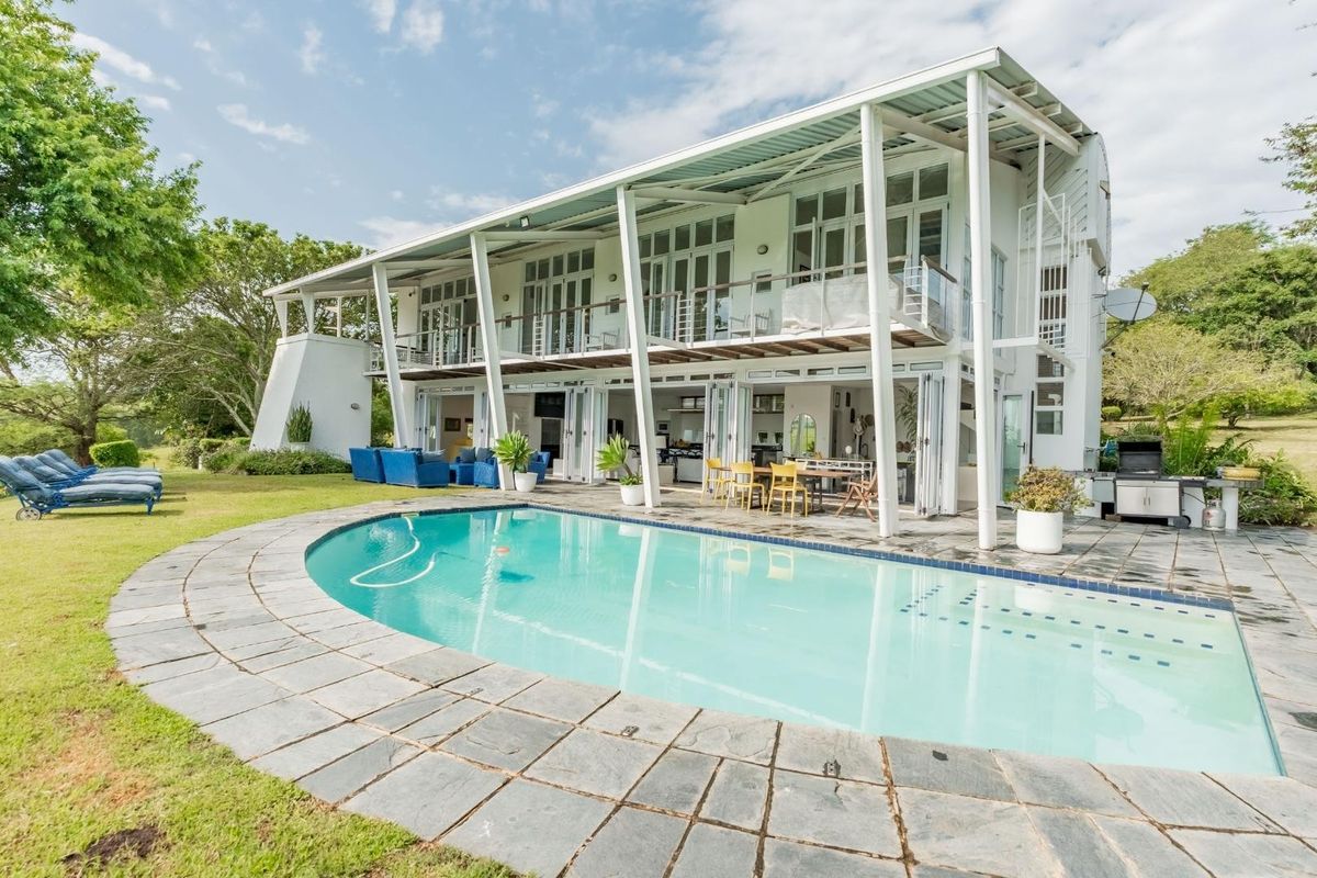 Rear view of a modern farm residence featuring a swimming pool, stone deck, covered patio, and expansive bi-fold doors opening to the interior living space.