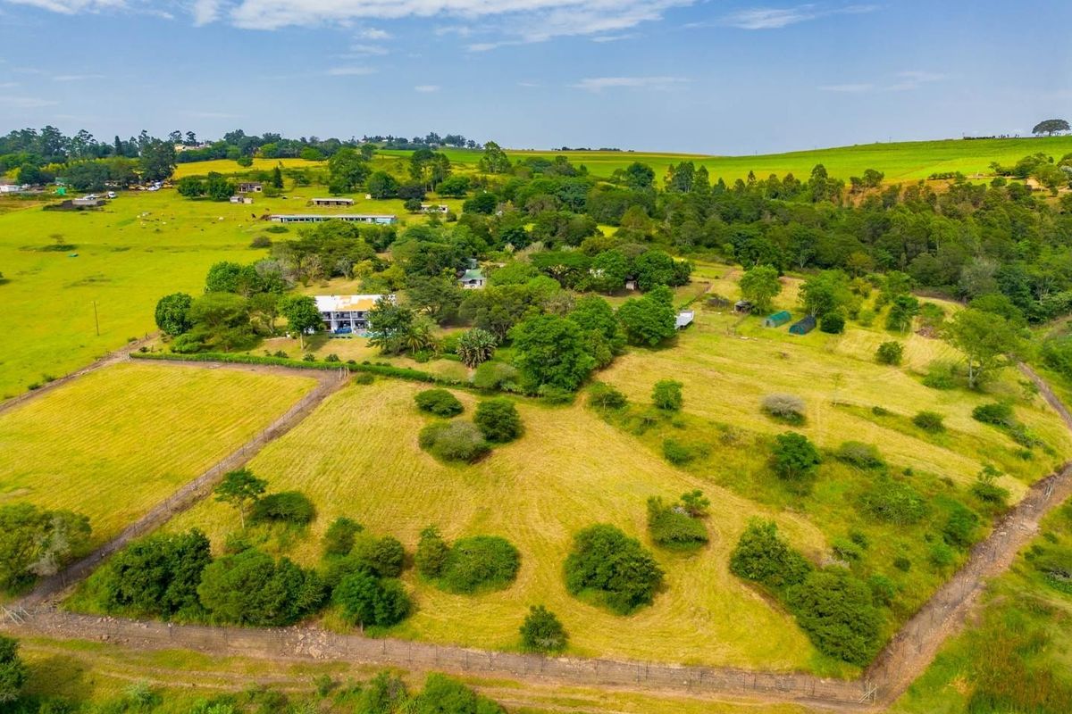 An aerial view of a large farm property featuring expansive green pastures, mature trees, and established perimeter fencing.