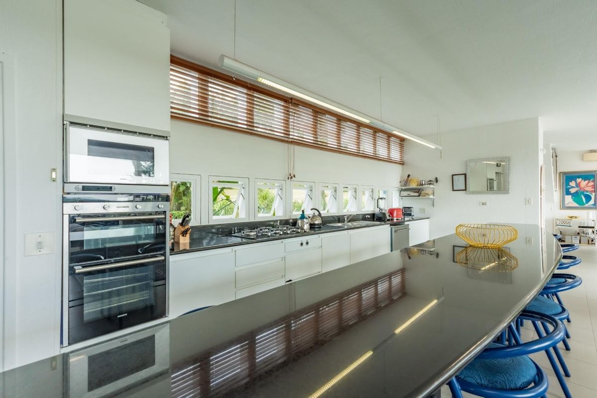 Modern kitchen featuring a long granite island, built-in double oven, gas hob, and extensive cabinetry with natural light from a row of windows.