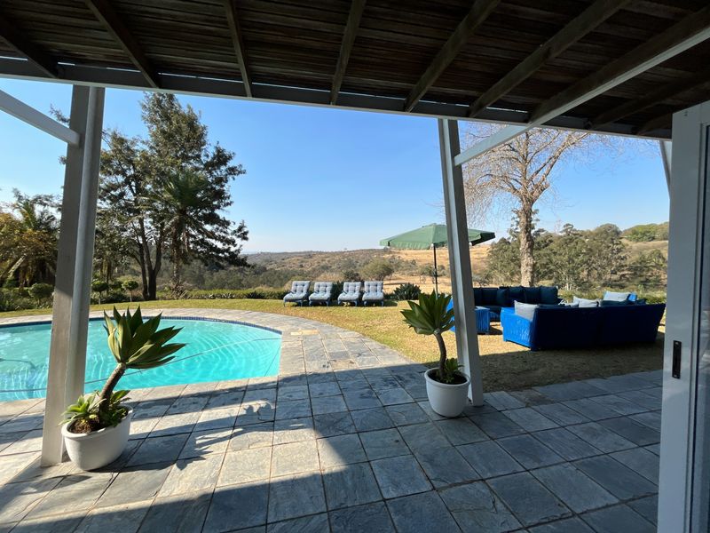 Covered patio area featuring stone paving and a timber pergola, overlooking a swimming pool and expansive rural landscape views.