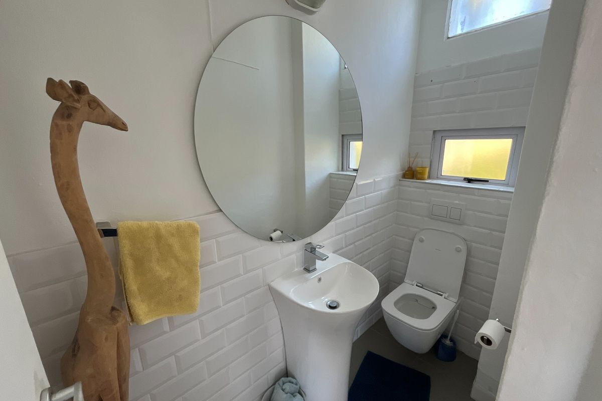 A compact, modern bathroom featuring a pedestal basin, wall-mounted toilet, and white subway tile wall finishes.