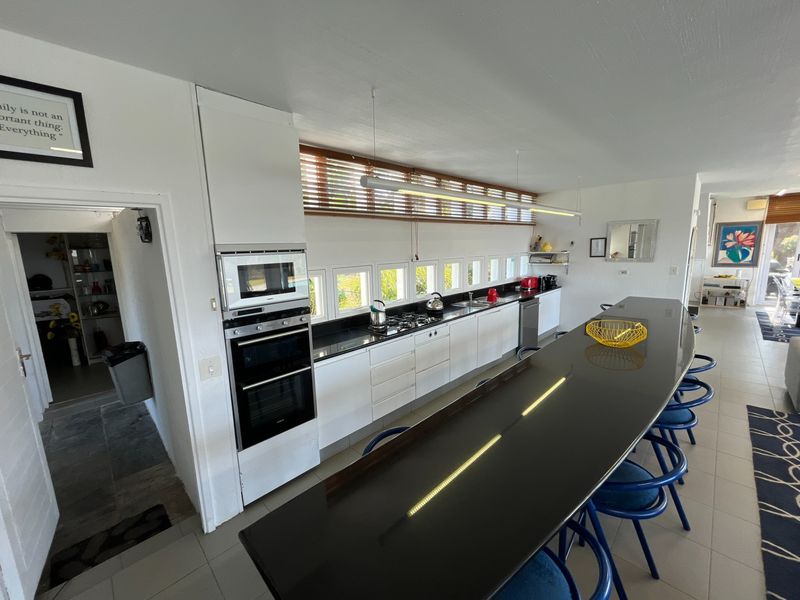 Modern kitchen featuring a long island with stone countertops, built-in oven, microwave, gas hob, and ample cabinetry, seamlessly connected to the living area.