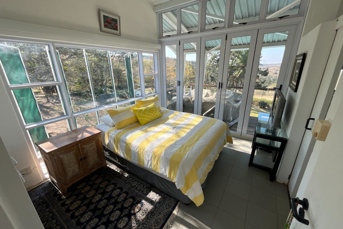 Bright bedroom featuring extensive glass windows and doors that provide natural light and scenic views, complemented by tiled flooring and a vaulted ceiling.