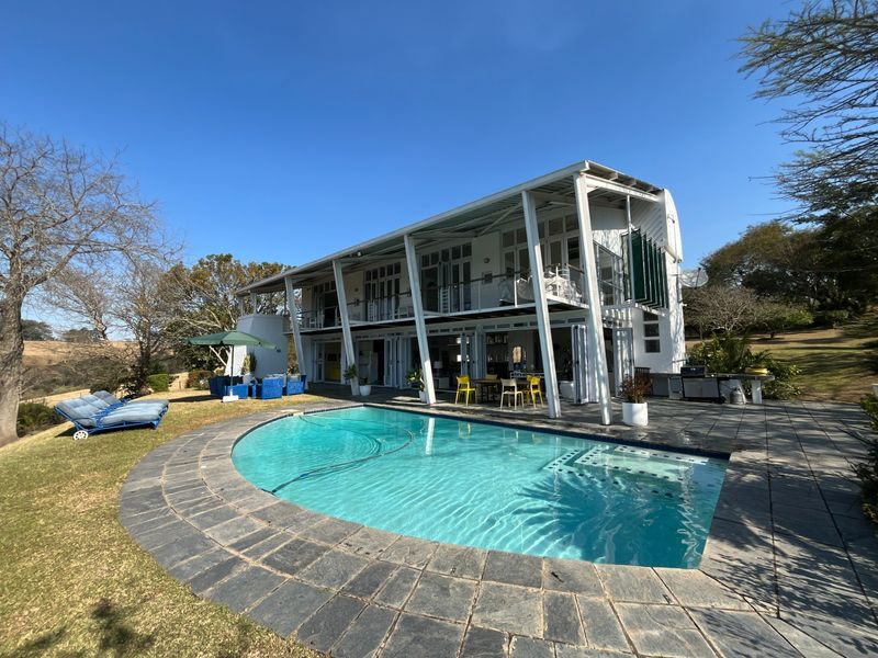 A modern two-story farm residence featuring a swimming pool with stone decking, a spacious covered patio, and expansive bi-fold doors opening to the garden.