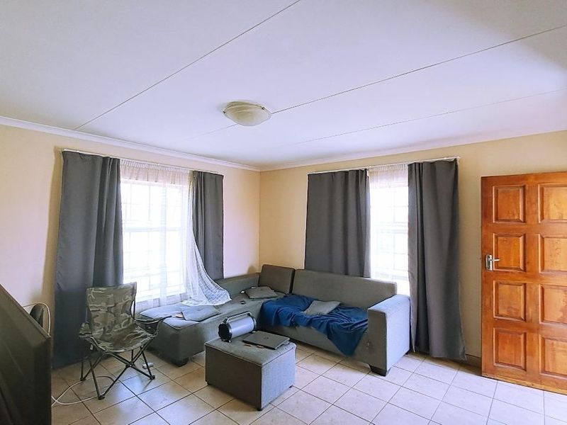 A functional living room featuring tiled flooring, a central ceiling light, and a solid wooden door, providing a neutral base for interior updates.