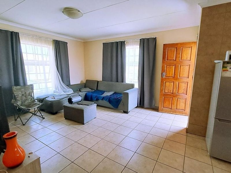 A living room featuring tiled flooring, a timber panel door, and natural light through large windows.