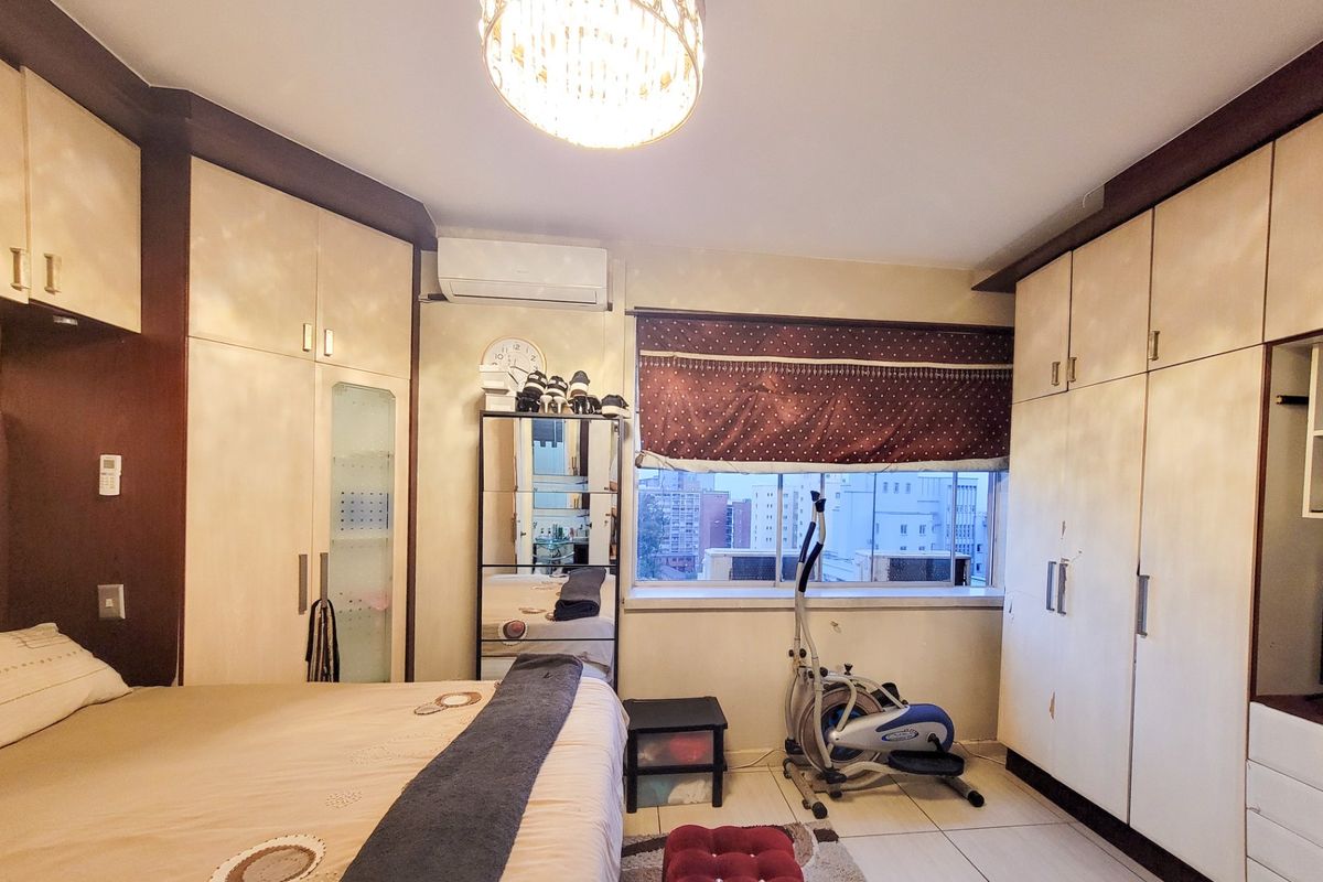 Bedroom featuring extensive built-in cabinetry, tiled flooring, and a wall-mounted air conditioning unit with views of the surrounding urban area.