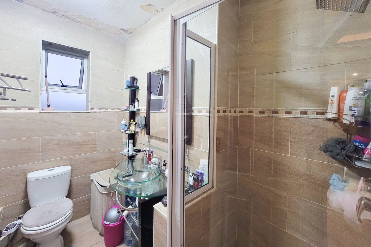 A bathroom featuring tiled walls, a glass vessel sink, and a shower enclosure. The ceiling shows signs of water damage and peeling paint.