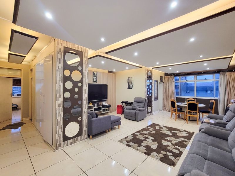 Spacious open-plan living and dining area featuring modern drop ceilings with recessed lighting, tiled flooring, and custom decorative wall paneling.