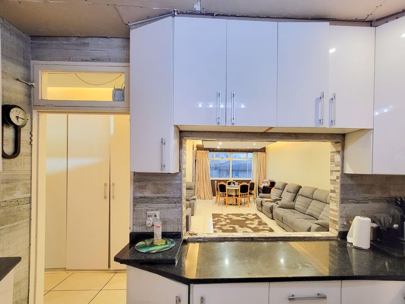 Open plan kitchen featuring white cabinetry and granite countertops, with a pass-through window connecting to the living and dining area.