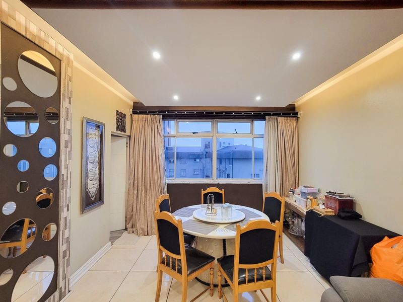 A dining area featuring tiled flooring, recessed ceiling lighting with cove accents, and a large window providing natural light.