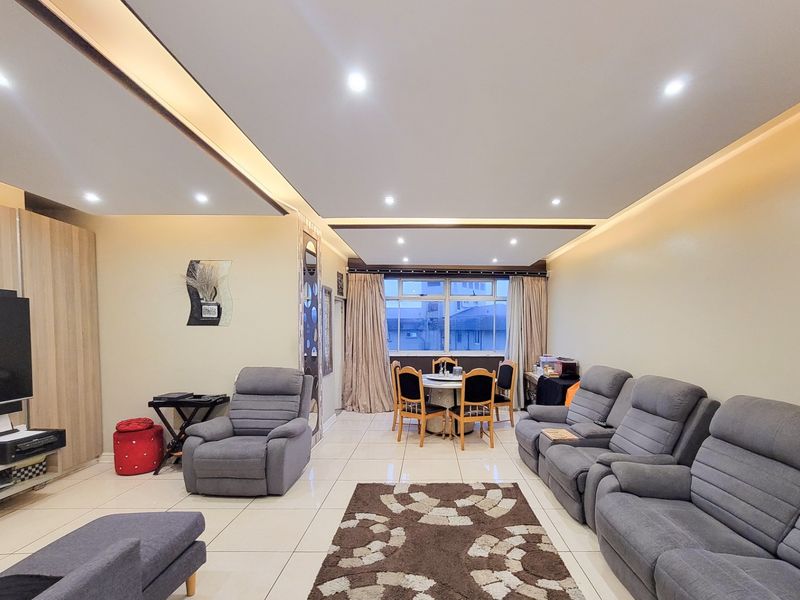Spacious open-plan living and dining area featuring modern recessed ceiling lighting, neutral tiled flooring, and large windows providing natural light.
