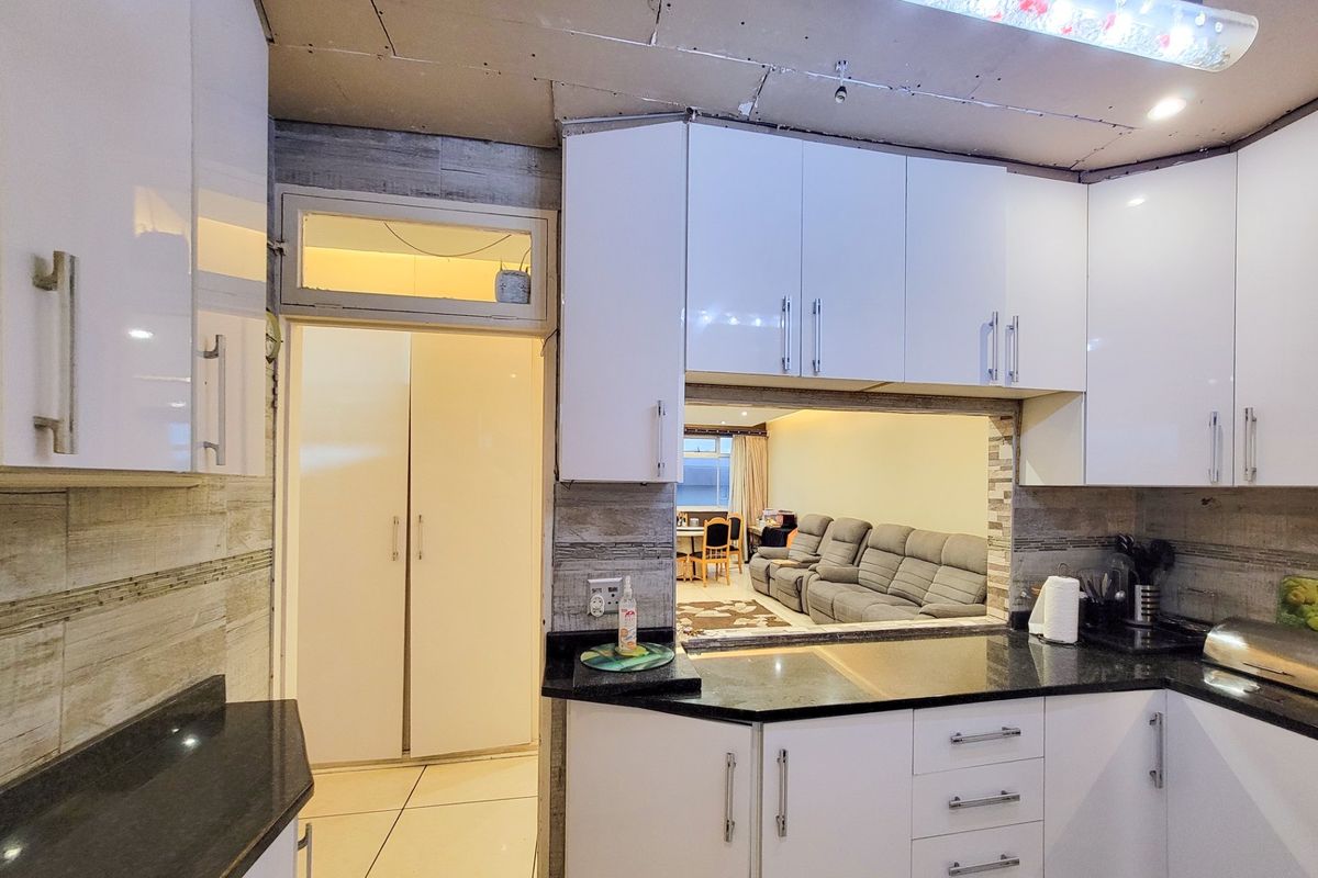 Kitchen featuring glossy white cabinetry and black granite countertops, with a pass-through window to the living area. The ceiling requires finishing.