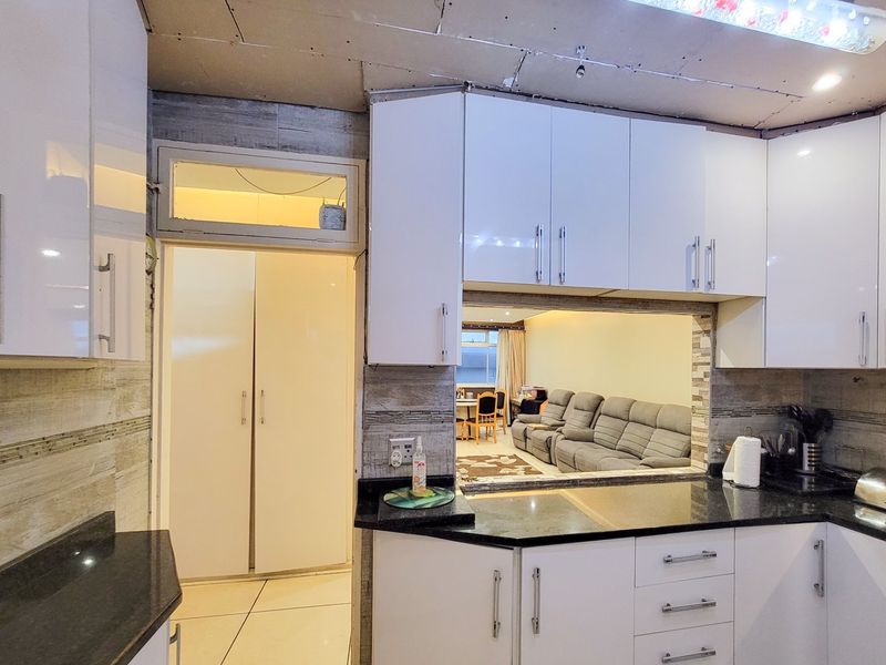 Kitchen featuring glossy white cabinetry and black granite countertops, with a pass-through window to the living area. The ceiling requires finishing.