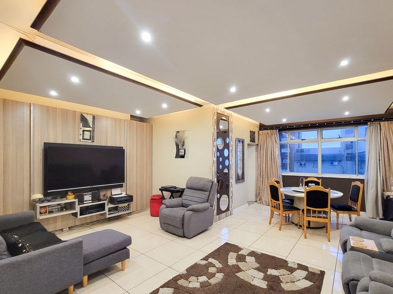 Spacious open-plan living and dining area featuring a modern drop ceiling with recessed lighting, tiled floors, and a custom built-in media wall.