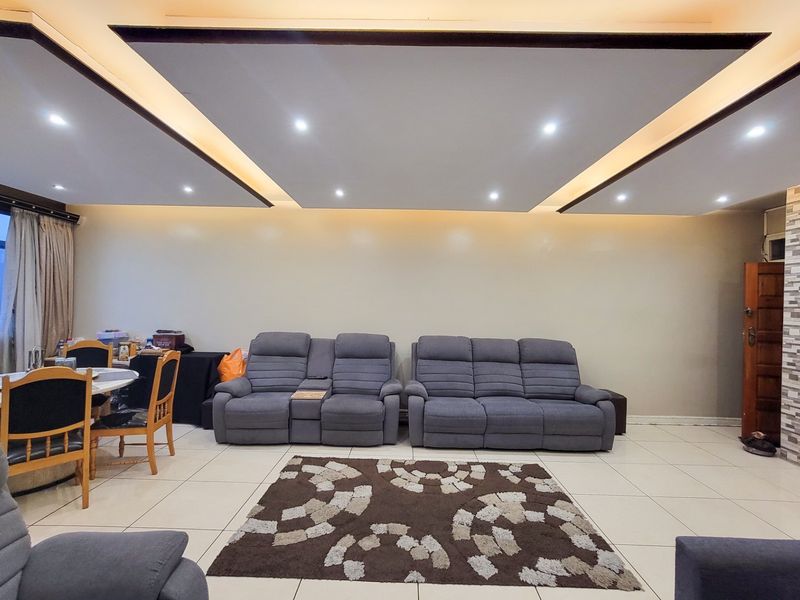 Spacious living area featuring a modern recessed ceiling with integrated cove lighting, tiled flooring, and a decorative stone-clad feature wall.