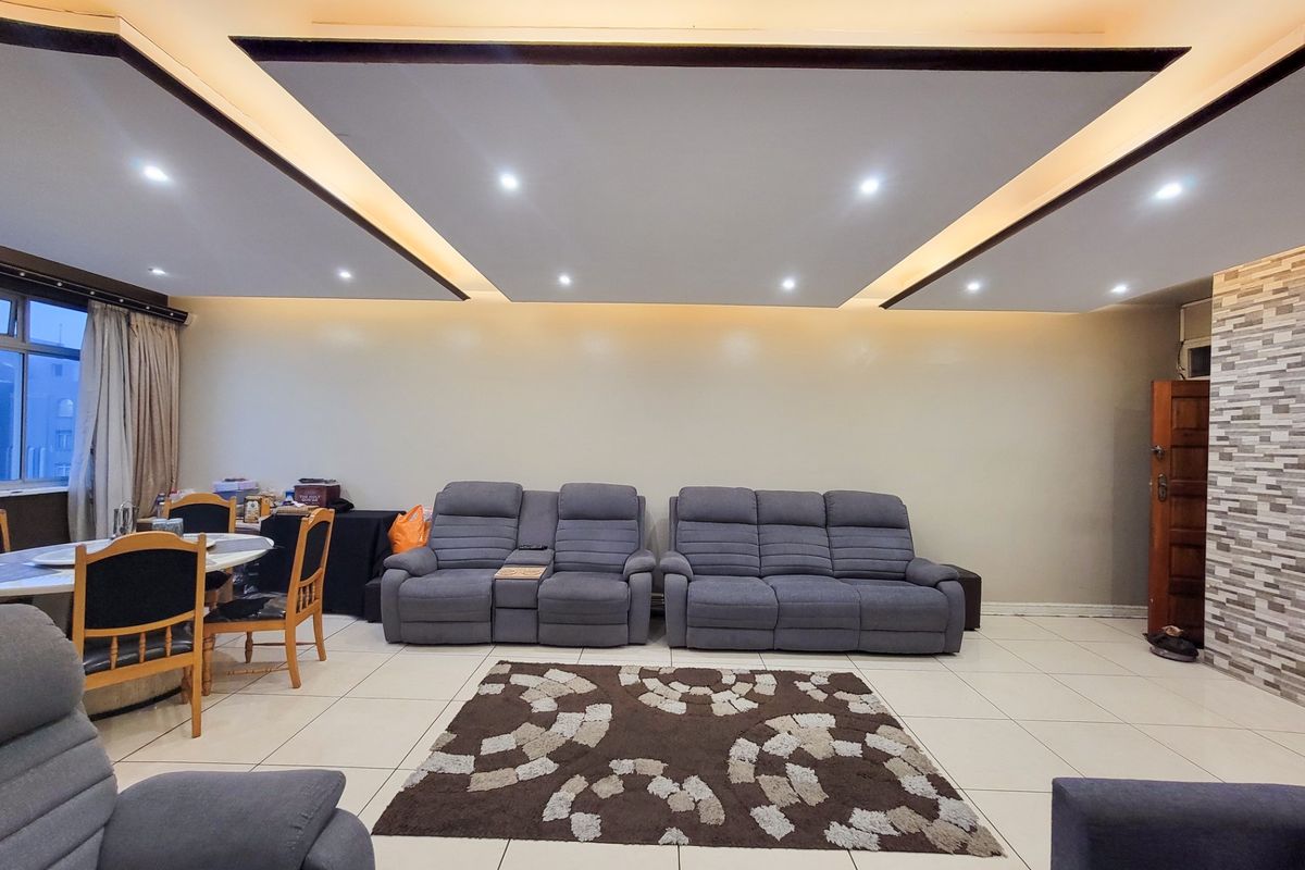 Spacious living area featuring a modern recessed ceiling with integrated cove lighting, tiled flooring, and a decorative stone-clad feature wall.