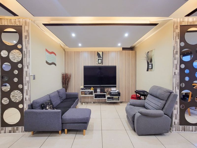 A living room featuring tiled flooring, a recessed ceiling with downlights, and decorative wood-look wall paneling surrounding the television area.
