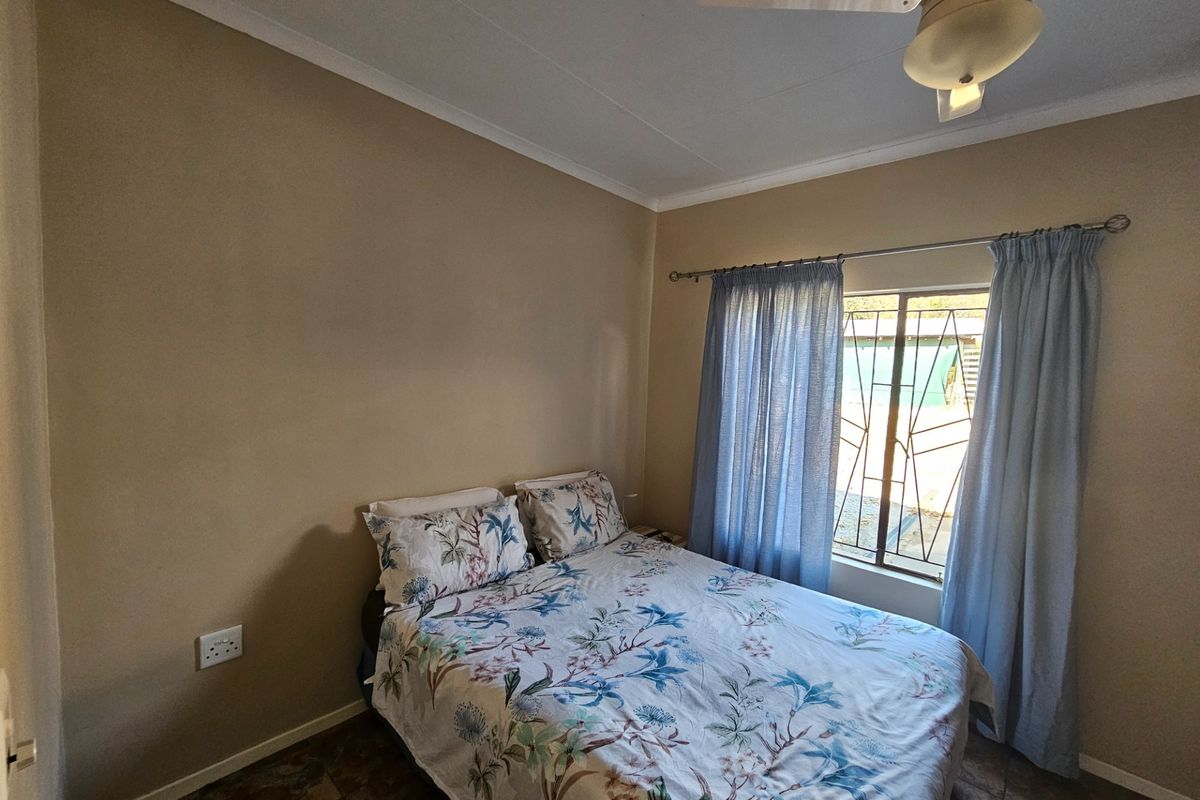 A functional bedroom featuring tiled flooring, a ceiling fan, and security bars on the window.
