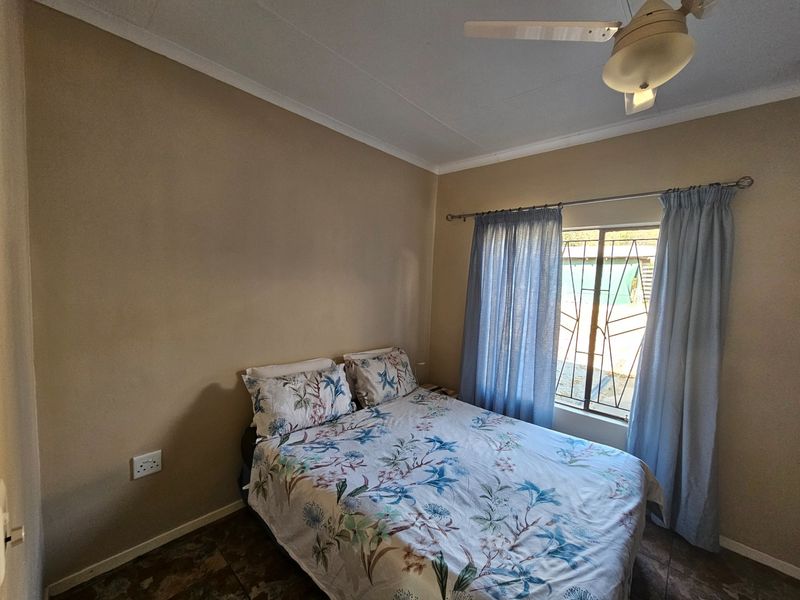A functional bedroom featuring tiled flooring, a ceiling fan, and security bars on the window.