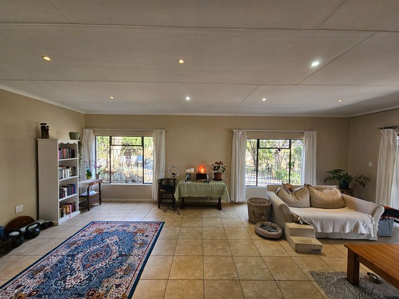 Spacious living room featuring neutral tiled flooring, recessed ceiling lighting, and large windows fitted with security bars, offering a bright and functional living space.
