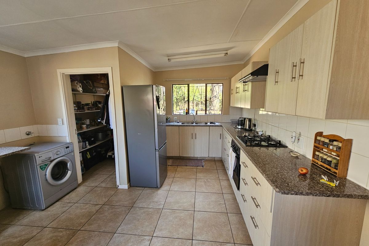 Functional kitchen featuring light wood cabinetry, granite countertops, gas hob, built-in oven, and an adjacent pantry area with tiled flooring throughout.