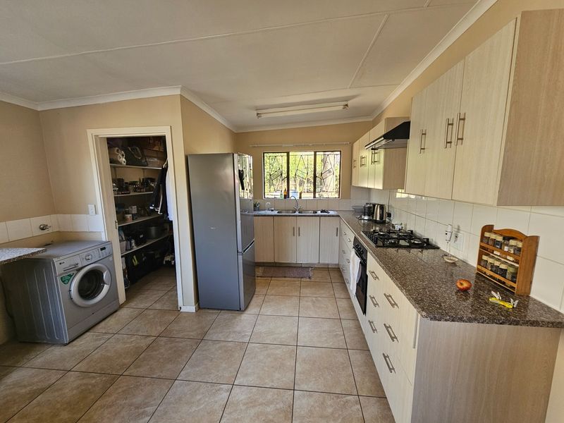 Functional kitchen featuring light wood cabinetry, granite countertops, gas hob, built-in oven, and an adjacent pantry area with tiled flooring throughout.