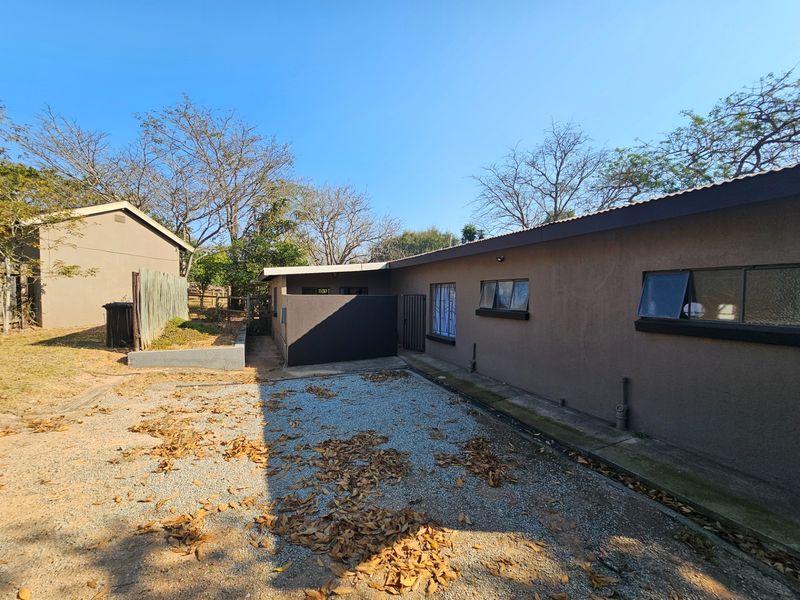 Rear exterior view of the property featuring a gravel driveway, concrete apron, and standard window installations with security bars.