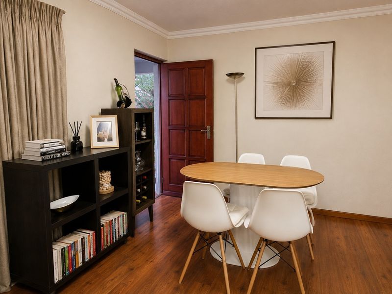 A well-maintained dining area featuring warm-toned laminate flooring, classic cornice detailing, and a solid timber door leading to an outdoor space.
