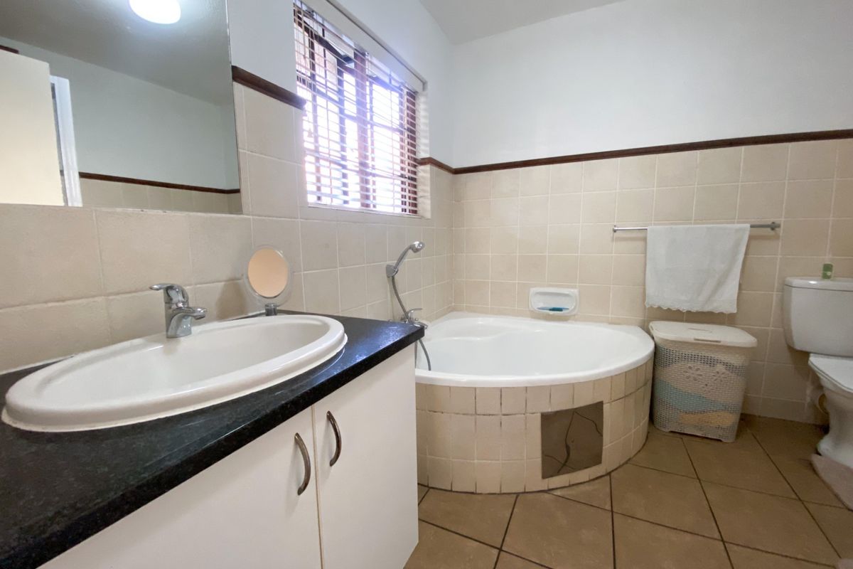 A functional bathroom featuring a corner bathtub, vanity with basin, toilet, and neutral wall tiling. The space is well-lit with natural light.