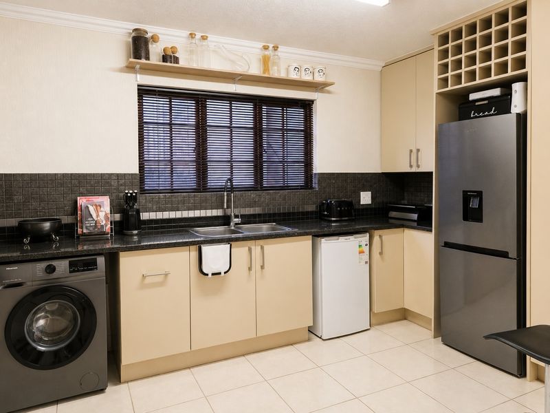 A well-maintained kitchen featuring neutral cabinetry, granite countertops, a tiled backsplash, and integrated space for laundry and refrigeration appliances.
