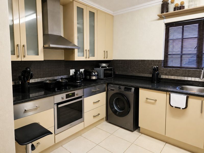 A functional kitchen featuring light-toned cabinetry, dark granite countertops, a built-in oven with extractor fan, and an integrated washing machine.