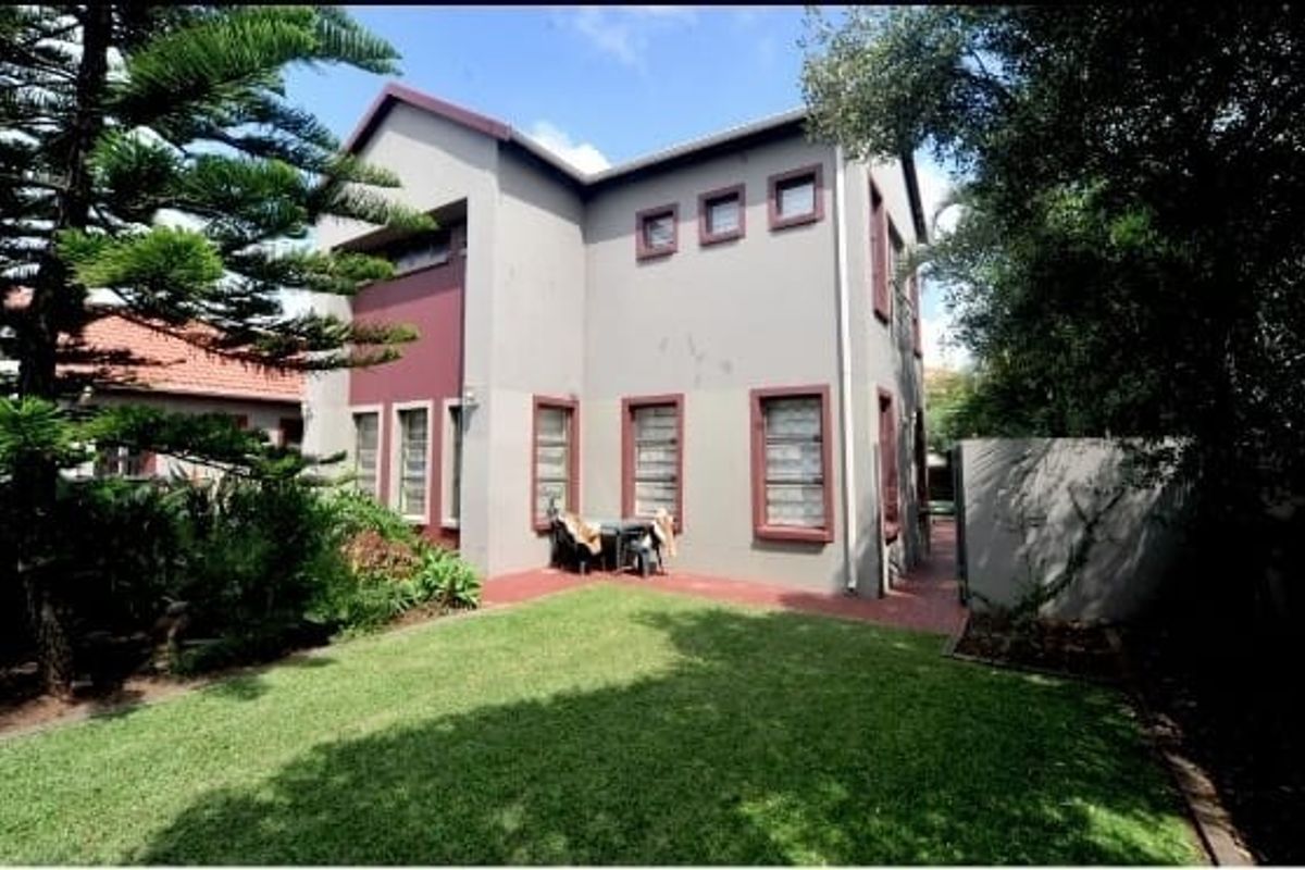 A view of the rear elevation of the double-story house, featuring a paved patio area, established garden, and lawn.