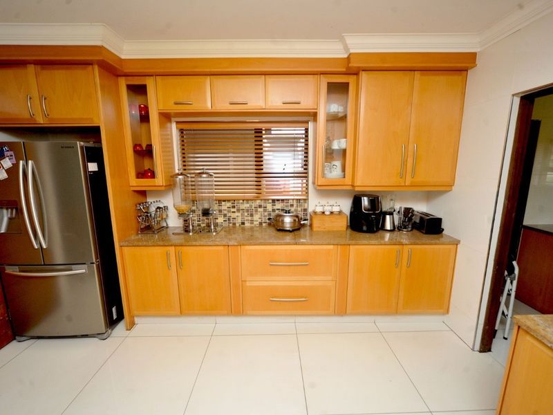 A functional kitchen featuring light wood cabinetry, granite countertops, a mosaic tile backsplash, and tiled flooring.
