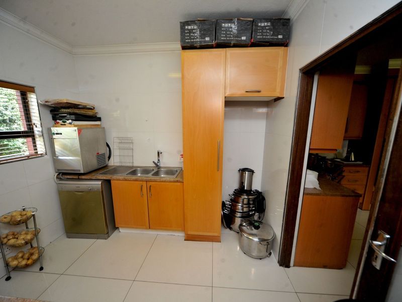 A functional scullery area featuring built-in wooden cabinetry, a double bowl stainless steel sink, and tiled finishes throughout.