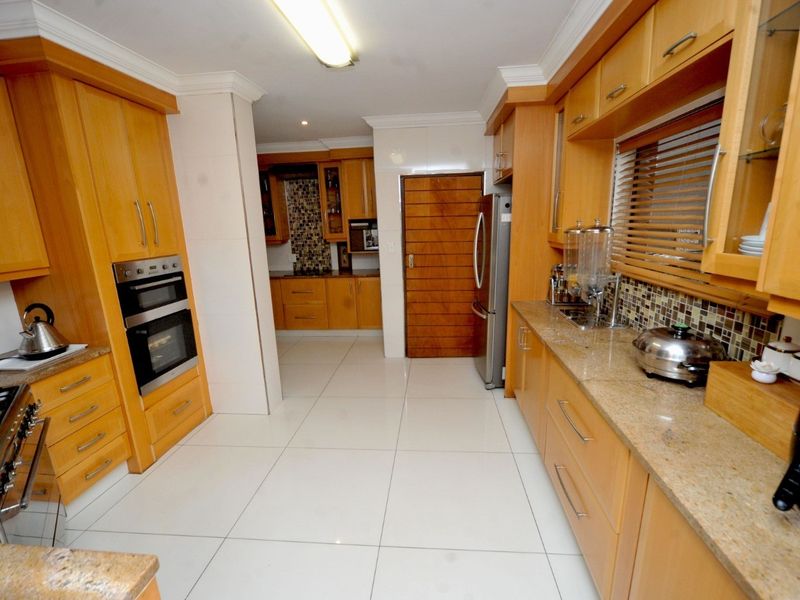 A spacious kitchen featuring light wood cabinetry, granite countertops, a built-in oven, gas hob, and modern tiled flooring with a mosaic backsplash.