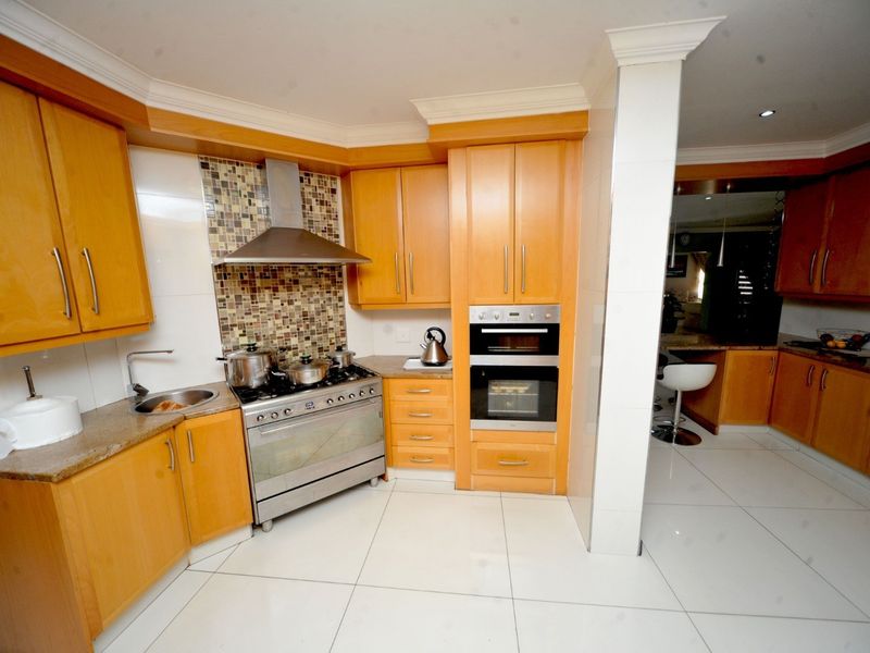 A functional kitchen featuring wooden cabinetry, granite countertops, a stainless steel gas stove with extractor, and a built-in double oven with tiled flooring.