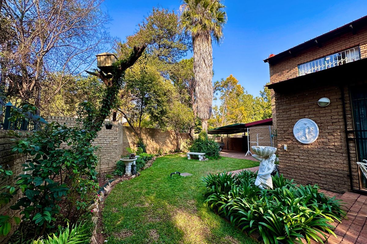 A private rear garden featuring established landscaping, brick boundary walls, paved pathways, and a covered carport area.